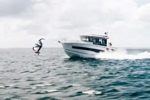 Un surfista en un hidrofoil levantándose del agua, mientras un bote pasa a gran velocidad a su lado.