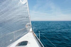 Vista del velero desde la proa, mostrando la vela ondeando y el mar azul en calma.