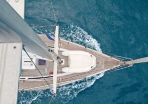 Vista aérea de un velero navegando sobre aguas azules, mostrando la cubierta de madera y la proa del barco.